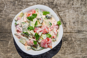 Fresh salad with tomato, cucumber, onion, parsley and mayonnaise on rustic wooden table