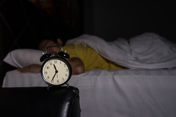 Alarm clock at 11:35 pm on bedside table in bed male sleeping in background, man rest in dark room...