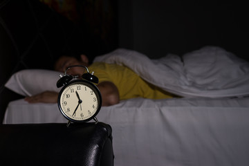 Alarm clock at 11:35 pm on bedside table in bed male sleeping in background, man rest in dark room at night
