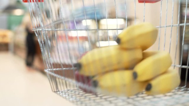 Closeup shot of shop's iron handcart with greengrocery products inside. Woman's white hands selection and buying quality vegetable, take a colorful peper in minimarket, pick up and puts in bag