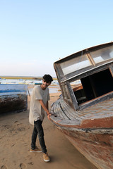 Young man posing next to an old boat