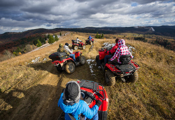 Top view of a group of people riding a off-road vehicles on a mountain road under a sky with clouds in autumn