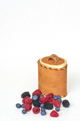Blueberries, raspberries and blackberries near bark basket on a white background