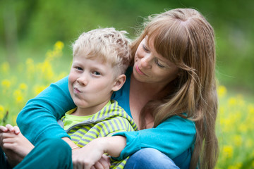 Caucasian mom and displeased son. A child in the arms of the mother, sitting on a summer meadow