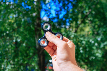 Hand with black steel rolling spinner. Green bokeh background.
