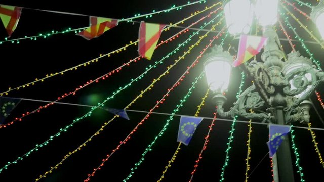 Camera movement from streetlight adronated by parties to flags and ornaments, illuminated at night