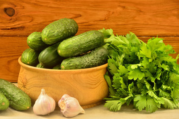 A bowl with cucumbers among parsley and garlic on a wooden background