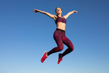 Fototapeta na wymiar Isolated of young happy sportswoman in sportswear jumping and flying at blue sky background. She enjoying summer. Healthy lifestyle concept, sport activity.