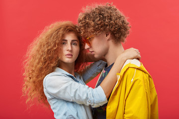 Indoor portrait of stylish young Caucasian couple in love spending time together after long separation. Red-haired male in shades looking at his beautiful girlfriend with passion and tenderness