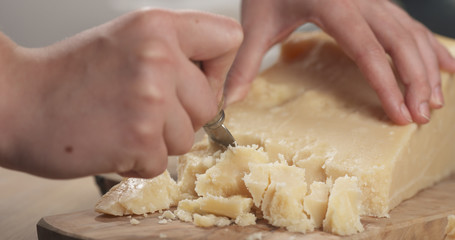 female hand cutting hard parmesan cheese