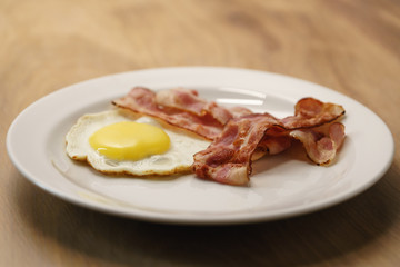 fried egg with crispy bacon stripes on plate