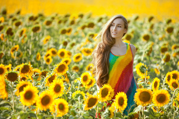 Fototapeta na wymiar Young woman is standing in a field among sunflowers.