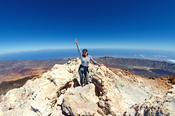 A hikking girl in grey trousers and sweater on the top of the volcano teide of Tenerife. From the side of the crater of a sleeping volcano. - obrazy, fototapety, plakaty