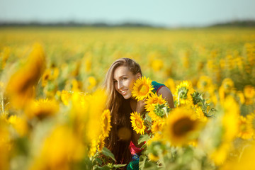 Young woman among yellow sunflowers in a field.