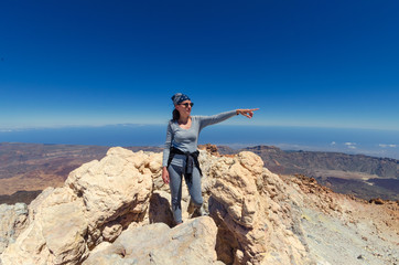 Obraz premium A hikking girl in grey trousers and sweater on the top of the volcano teide of Tenerife. From the side of the crater of a sleeping volcano.