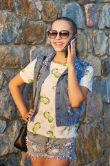 Girl talking on mobile phone on stone wall background