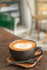 Hot latte coffee with latte art in a matt black cup on the wooden table in a coffee shop background.