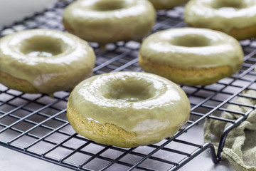 Fresh baked matcha banana donuts with matcha glaze, on cooling rack, horizontal