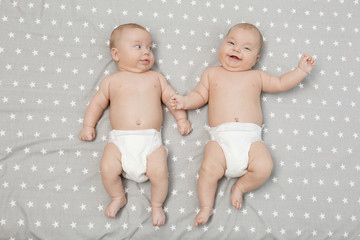 Beautiful baby twins lying together on bed sheet