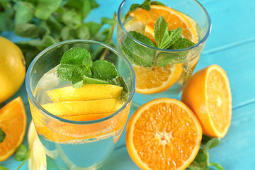 Glasses of fresh lemonade with citrus fruits on color background