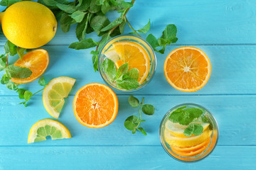 Glasses of fresh lemonade with citrus fruits on color background