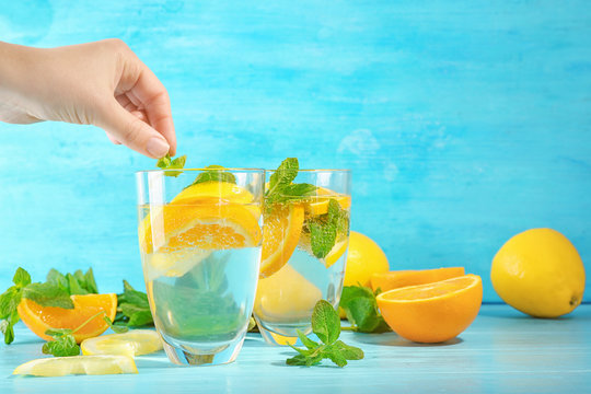 Young woman dropping mint into glass of fresh citrus lemonade on color background