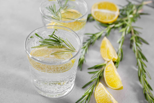 Glass of fresh lemonade with rosemary on grey background