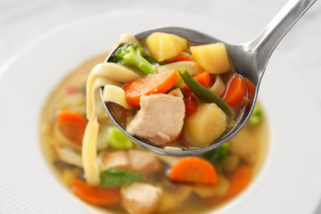 Ladle with turkey soup over plate, close up