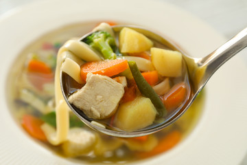 Ladle with turkey soup over plate, close up