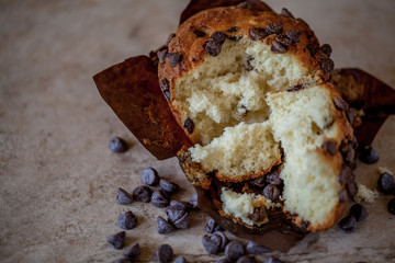 Fresh broken chocolate chip muffin on a brown background