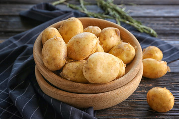 Bowls with raw organic potato on wooden table
