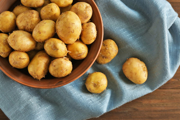Bowl with raw organic potato on wooden table