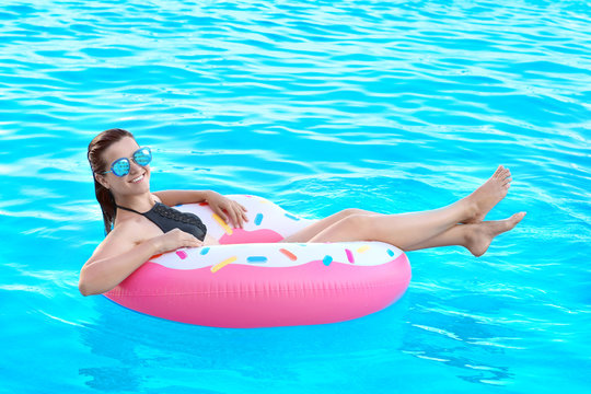 Beautiful young girl with inflatable donut in blue swimming pool