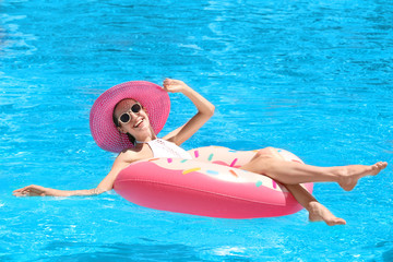 Fototapeta na wymiar Beautiful young woman with inflatable donut in blue swimming pool