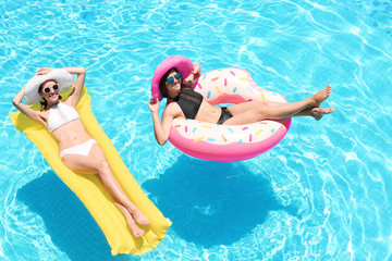 Beautiful young women with inflatable donut and mattress in blue swimming pool