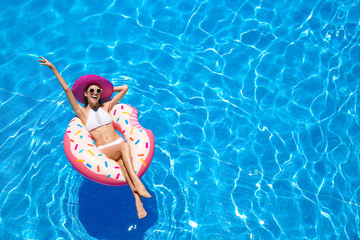 Naklejka premium Beautiful young woman with inflatable donut in blue swimming pool