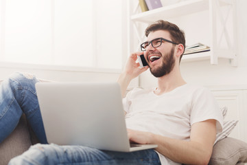 Smiling young man at home with laptop and mobile
