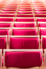 Fototapeta premium Rzędy pustych, czerwonych, aksamitnych siedzeń wewnątrz kościoła, stadionu, teatru czy sali koncertowej rozciągają się w dal i wypełniają kadr.