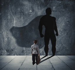 Young businessman with his shadow of super hero on the wall. Concept of powerful small man