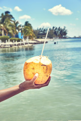 Fototapeta na wymiar Fresh coconut drink directly from the fruit / Hand of black woman holding coconut with drinking straw at caribbean coast
