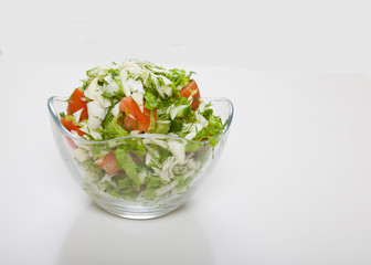 Salad of tomatoes, cabbage and cucumbers in a glass bowl is on a white table