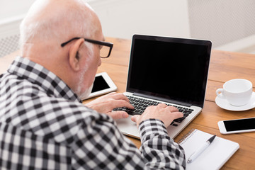 Senior man using laptop with blank screen mockup