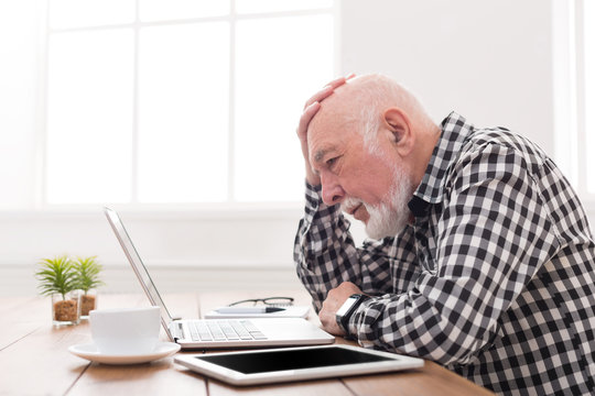 Worried senior man using laptop at home