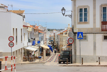 Fototapeta na wymiar Typical european touristic small town street, Lagos Algarve coast, Portugal. Traditional historic old town city architecture lifestyle summer scene with local people, street signs and ocean background