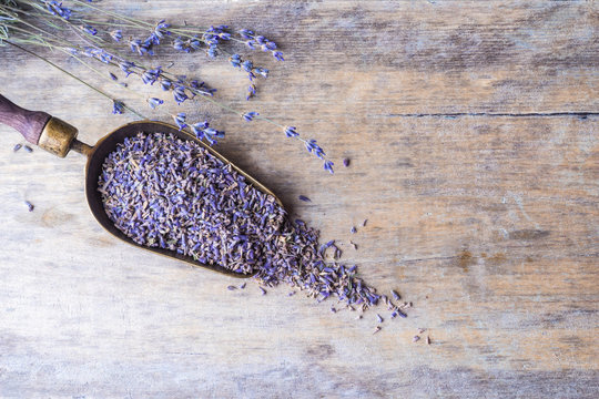 Lavender flowers in an antique scoop on wooden background. Top view.