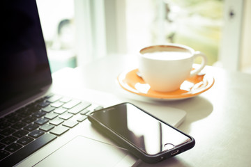 Cup of coffee and smart devices on the table close up. (Processed in vintage colour tone)