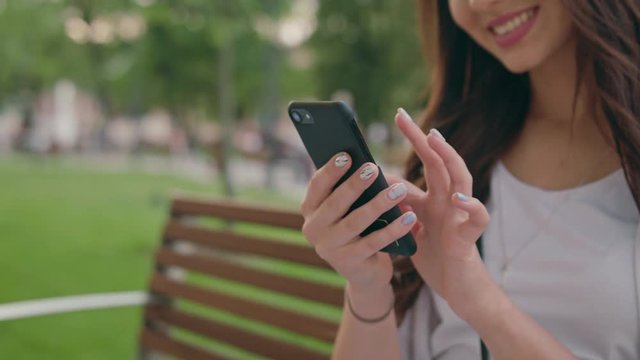A beautiful brunette young lady using a smapthone outdoors sitting on a bench in the park. Soft focus. Dolly shoot