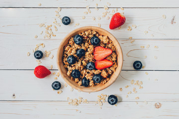 Homemade granola and fresh berries on wood table with space.