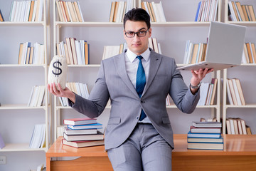 Businessman in library with a money sack and a laptop