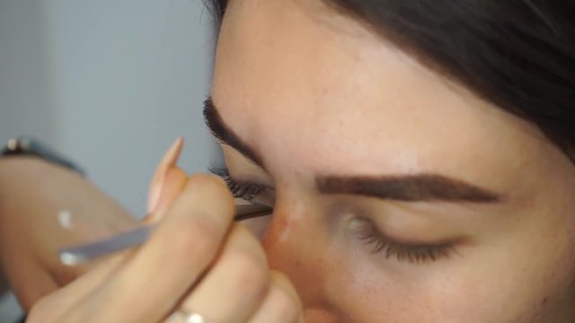 Glue artificial eyelashes Eyelash extensions, the make-up artist takes with the help of forceps and imposes artificial eyelashes on the woman's eyes. The process of eyelash extension for make-up